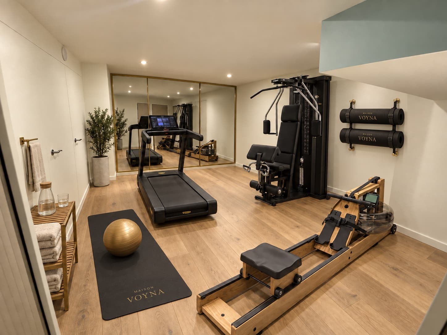 La salle de sport : tapis de course, rameur de bois, miroir à cadre de laiton et linge marqué Maison Voyna.
